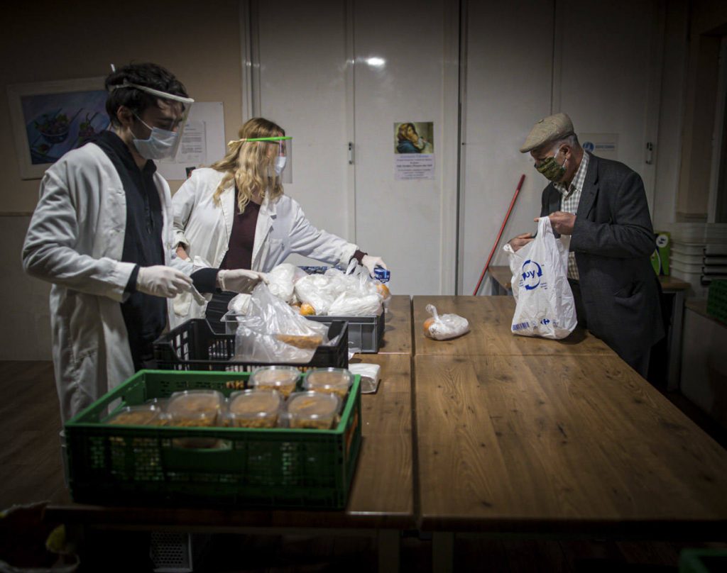 voluntarios en un comedor social atendiendo a una persona mayor